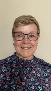 A woman with glasses and short hair wearing a floral shirt.