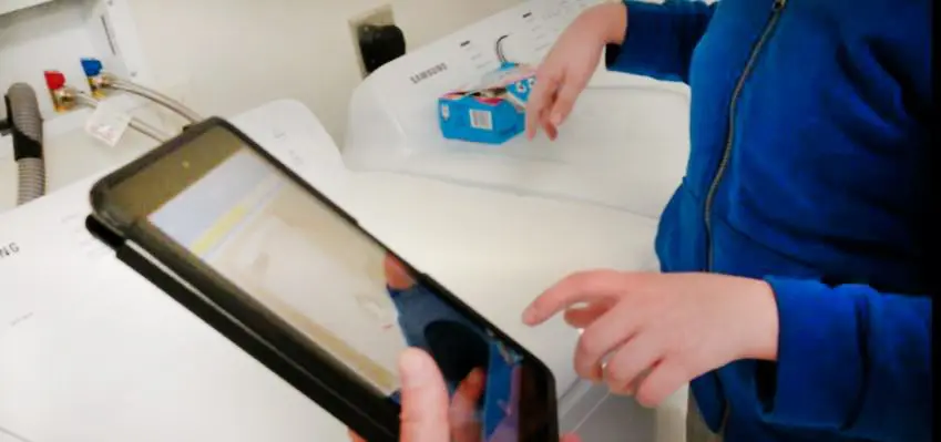 A person in a blue jacket using a smartphone to scan a barcode on a product box in a store.