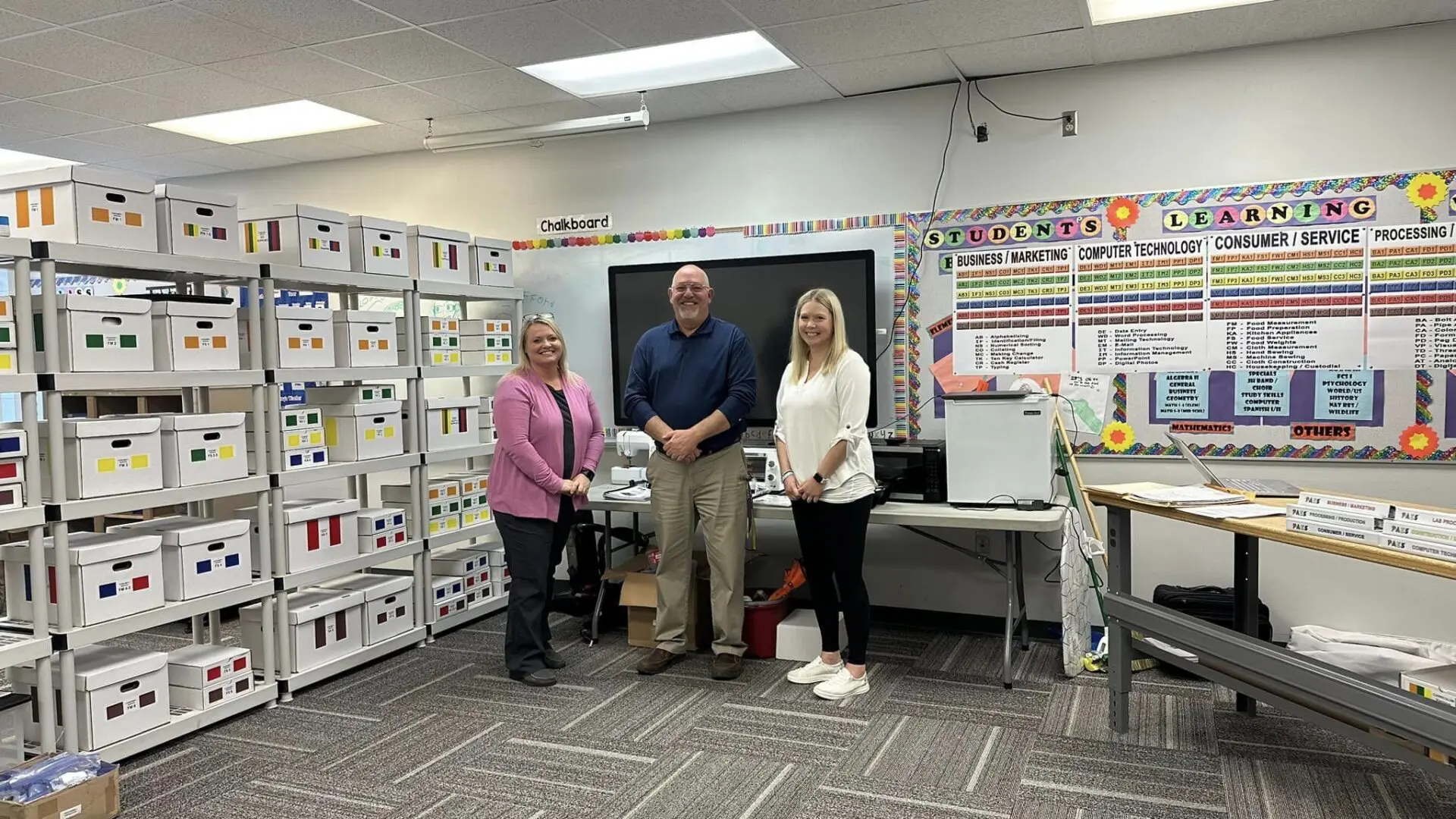 Three people standing in a room with boxes.