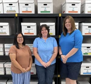 Three women standing in front of a wall full of boxes.