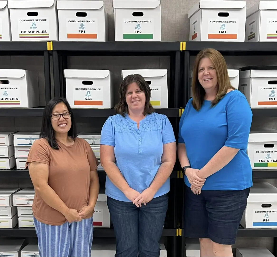 Three women standing in front of a wall full of boxes.