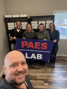 Group holding PAES LAB sign, smiling.