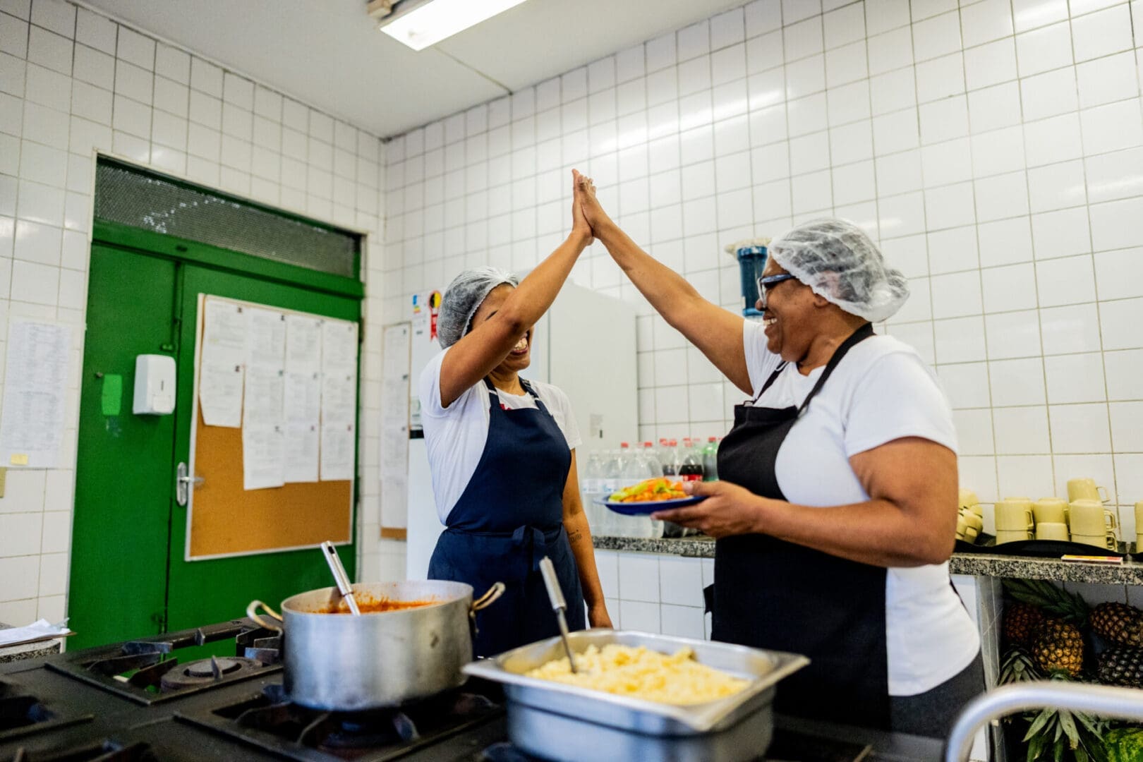 Cooks high-fiving in kitchen with food.
